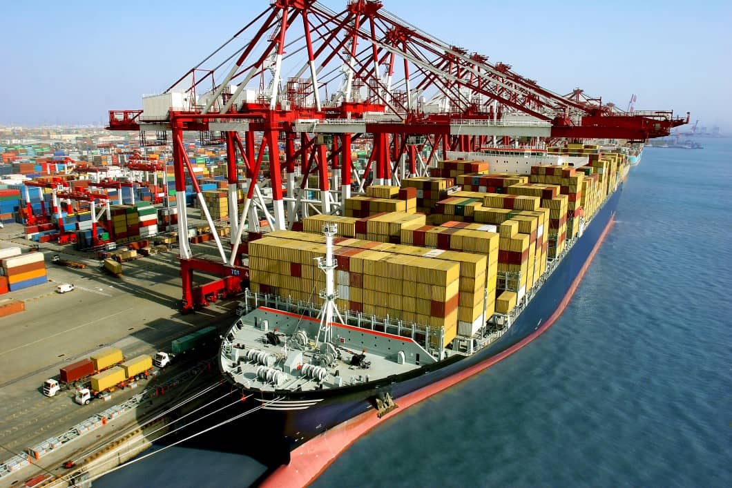 A container ship docked at port and ready for unloading. Trucks are waiting to dray containers away.